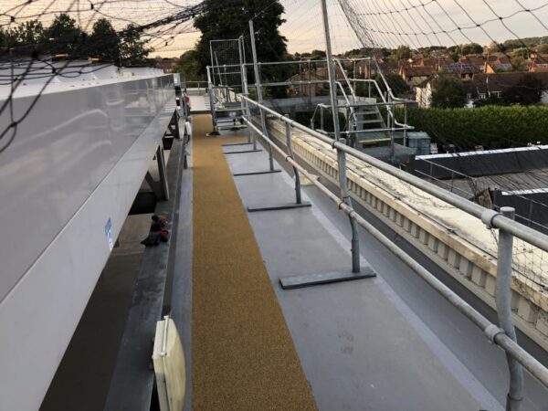 Walkway along a flat roof edge beside guardrails and rooftop equipment