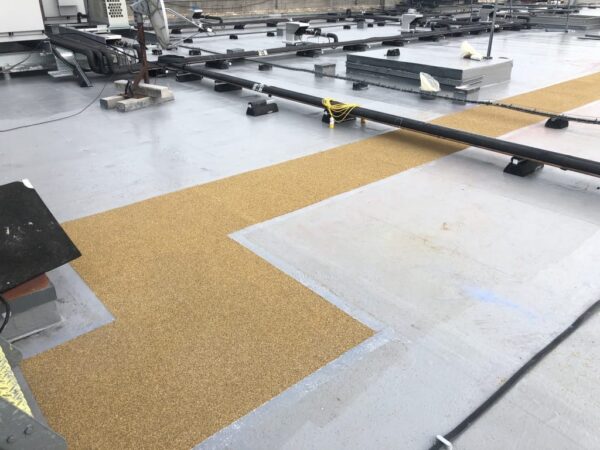 Textured walkway route turning across a liquid-applied flat roof