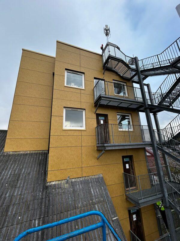 Sandstone-colored rainscreen wall with windows and external steel stairs