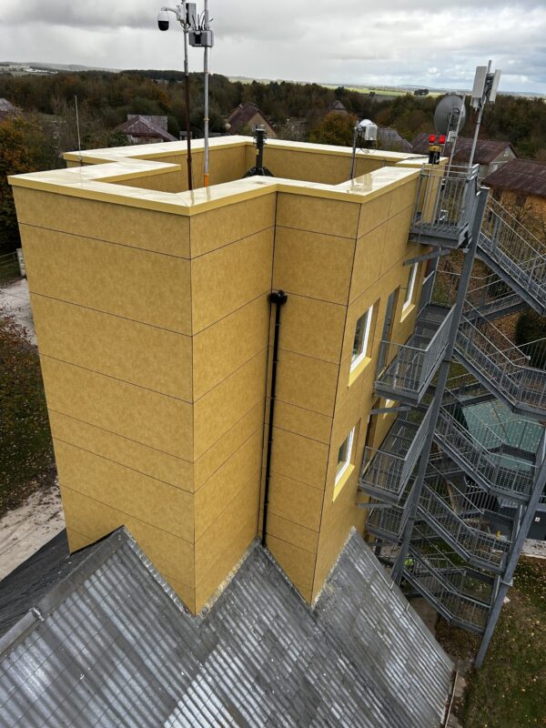 Parapet and wall of a building reclad in sandstone-colored rainscreen panels