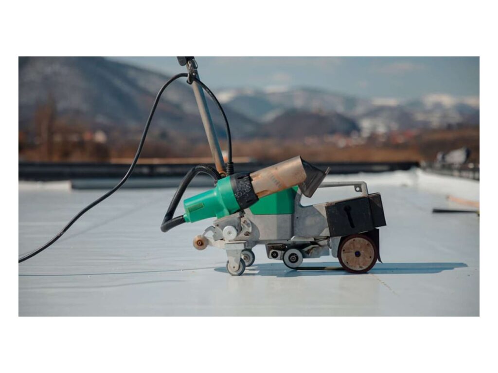 Welding machine seaming a light membrane on an installed roof with mountains behind