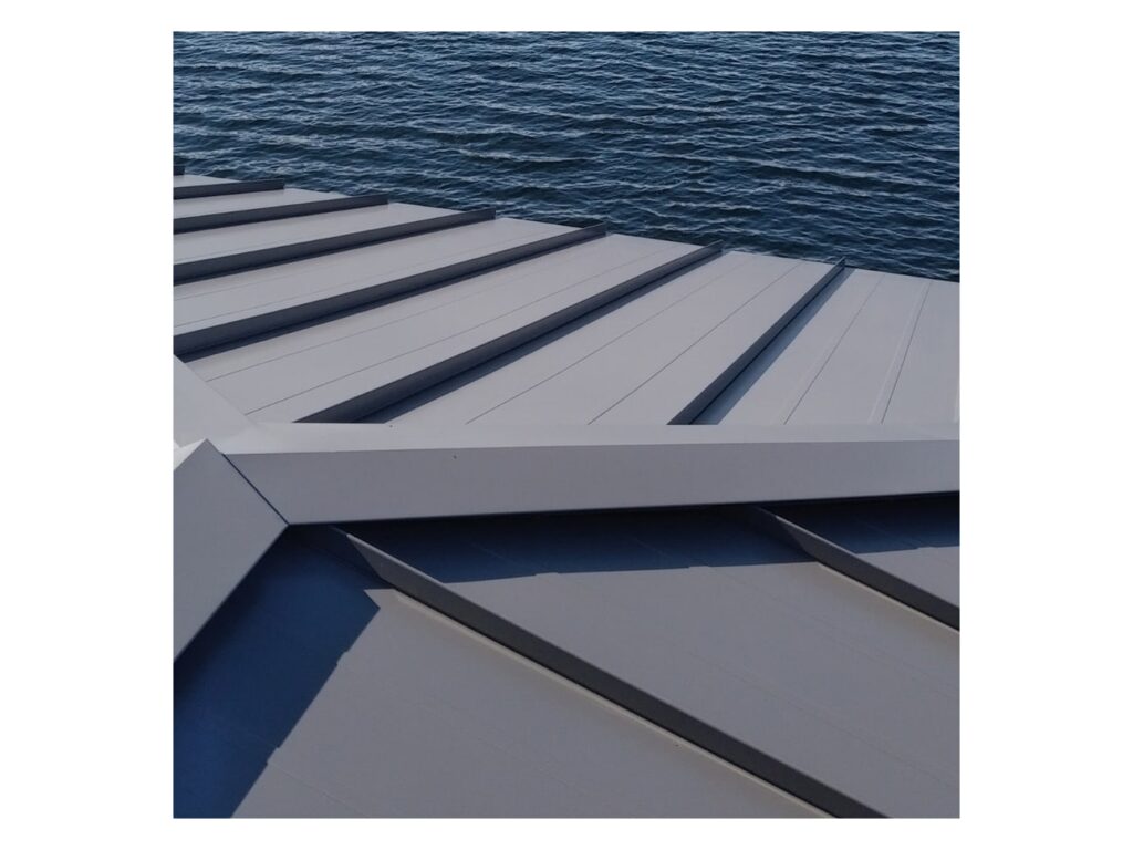 Gray standing seam metal roof panels installed on a building above dark water